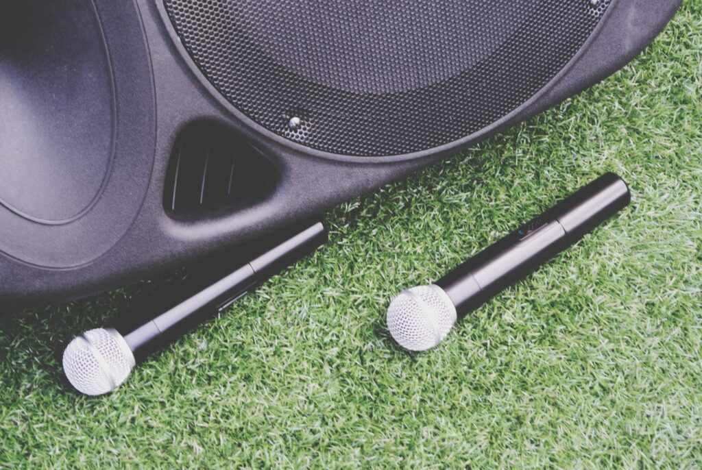 Close-up of two wireless microphones lying on grass next to a large PA speaker—ideal for outdoor events, speeches, and mobile announcements.
