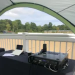 Event equipment setup under Coleman shelter with table, audio gear and microphone for outdoor use
